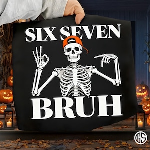 May include: Black tote bag with a Halloween design. It features a skeleton wearing an orange cap, with the words "SIX SEVEN BRUH" in white. The skeleton is making an "OK" hand gesture and pointing. Pumpkins and lanterns are in the background.