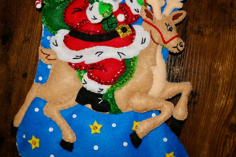 May include: A Christmas stocking with a blue background and white polka dots. Santa Claus is riding a reindeer with a red harness. The reindeer is brown with black hooves. There are yellow stars on the stocking.