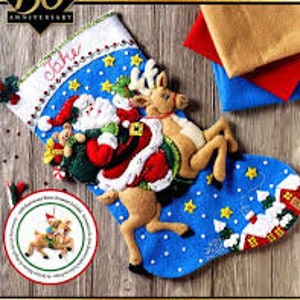 May include: A blue felt Christmas stocking with a Santa Claus and reindeer design. Santa is carrying a bag of gifts and a teddy bear. The reindeer is pulling a sleigh with a small house in the background. The stocking is personalized with the name "Jake".