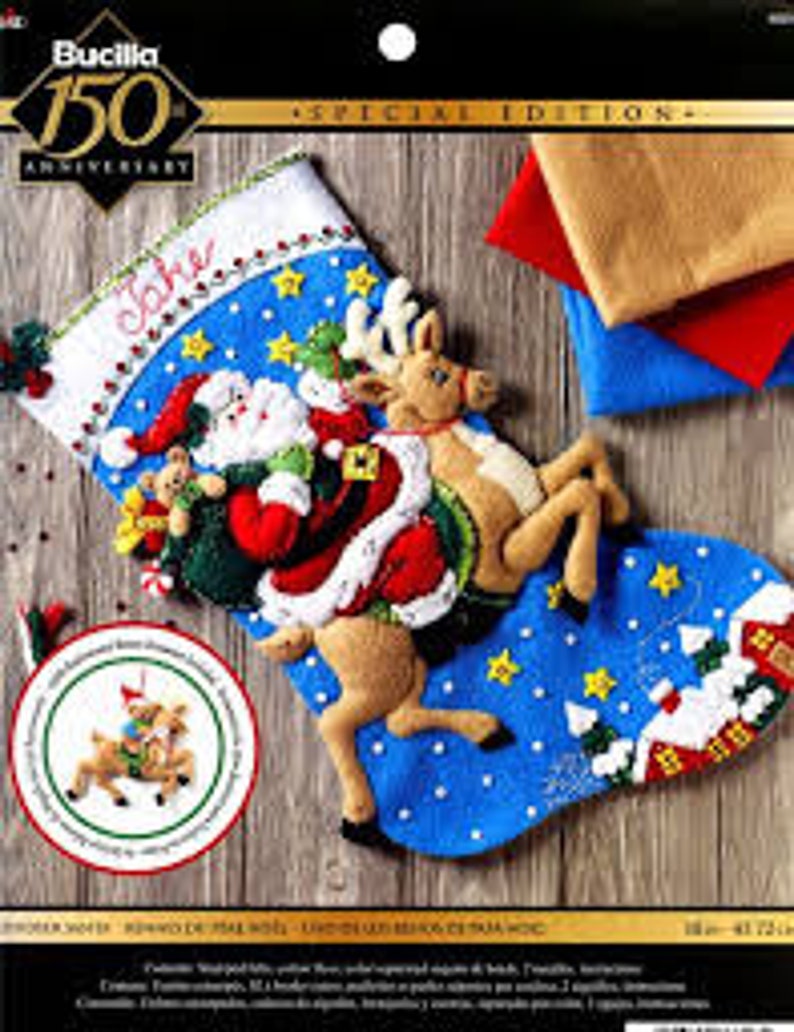 May include: A blue felt Christmas stocking with a Santa Claus and reindeer design. Santa is carrying a bag of gifts and a teddy bear. The reindeer is pulling a sleigh with a small house in the background. The stocking is personalized with the name "Jake".