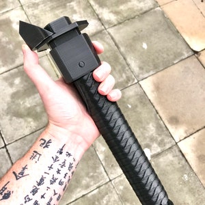 Puede incluir: Un sable de luz negro impreso en 3D con un mango texturizado y una hoja negra. El sable de luz se sostiene en la mano de una persona.