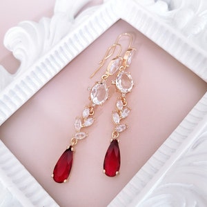 May include: A pair of gold dangle earrings with clear crystal stones and red teardrop-shaped stones.