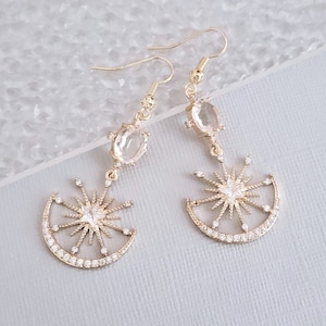 May include: Gold tone earrings with a crescent moon and star design. The earrings feature clear crystal accents and a dangling oval-shaped crystal.