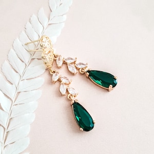 May include: A pair of gold-tone drop earrings featuring a filigree post, a branch-like design adorned with clear marquise-cut stones, and a large, faceted, pear-shaped emerald green crystal pendant at the base of each earring.