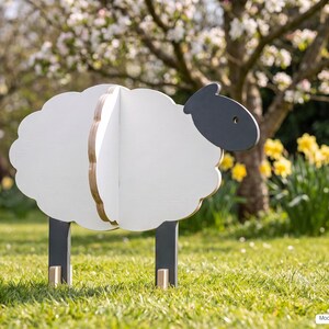 May include: A three-dimensional sheep figure constructed from flat wooden panels. The body is white with scalloped edges, while the head and legs are dark gray. The edges of the wood panels show a natural light brown layered plywood texture.