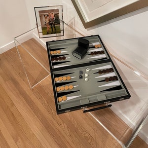 May include: A black backgammon set with wooden playing pieces and dice on a clear acrylic table. A framed photo of a family is on the table.