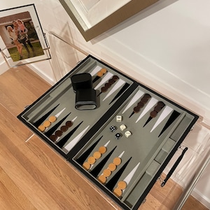 May include: A black backgammon set with a gray felt playing surface, wooden playing pieces, and dice. The set is open and ready to play.