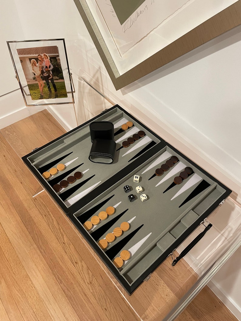 May include: A black and gray backgammon game set with a leather carrying case. The game board is open and shows the pieces in play. The dice are on the board and show the numbers 4 and 6.