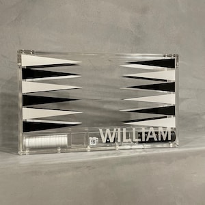 May include: A clear acrylic backgammon game set with black and white triangles. The set includes a clear acrylic tray with a black and white checkerboard design, white chips, and black dice. The name "WILLIAM" is printed on the front of the tray.