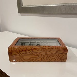 K&ouml;nnte beinhalten: Eine Holzuhrbox mit Glasdeckel. Die Box hat eine Holzmaserung und das Wort "Time" ist in das Glas graviert.