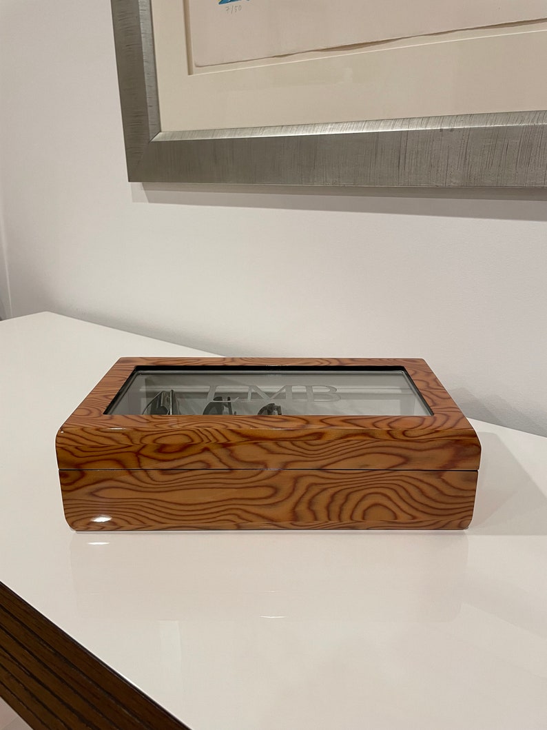 K&ouml;nnte beinhalten: Eine Holzuhrbox mit Glasdeckel. Die Box hat eine Holzmaserung und das Wort "Time" ist in das Glas graviert.
