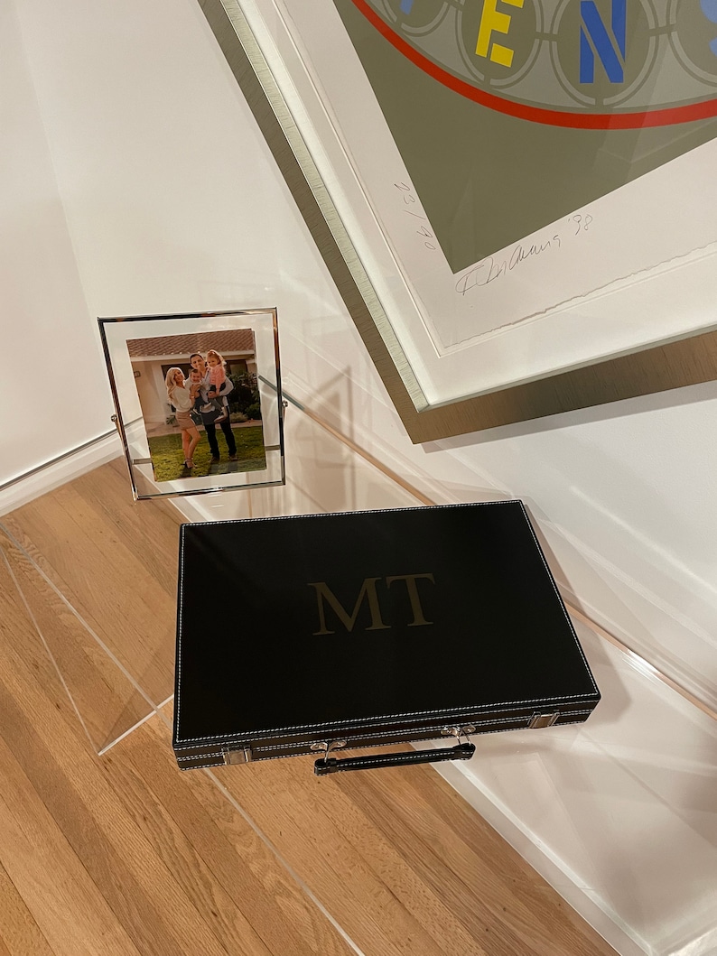 May include: A black leather game case with a gold embossed "MIT" logo and a silver handle. The case is sitting on a wooden floor.
