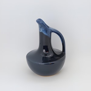 May include: A dark blue ceramic pitcher with a light blue glaze on the top. The pitcher has a rounded body and a curved handle.