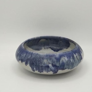 May include: A ceramic bowl with a wide, shallow design. The bowl features a white interior and a blue exterior with a textured, dripped glaze effect. The bowl is a decorative piece.