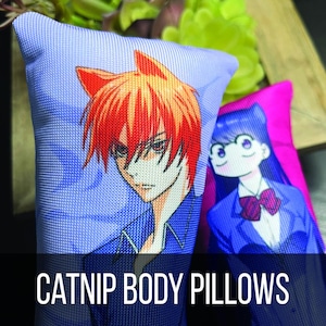 Puede incluir: Dos almohadas para gatos con diseños de personajes de anime. Una almohada presenta un personaje pelirrojo con apariencia de zorro, la otra un personaje con pelo largo azul y gafas. Las almohadas son azules y rosas.
