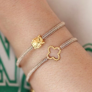 Könnte beinhalten: Zwei Armbänder mit goldenen Anhängern. Ein Anhänger ist ein Marienkäfer und der andere ein vierblättriges Kleeblatt.