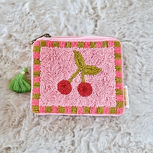 May include: A square zipped pouch featuring a beaded cherry design in red and green on a light pink background. The border consists of alternating pink and olive green beaded squares. A green tassel is attached to the metal zip pull.