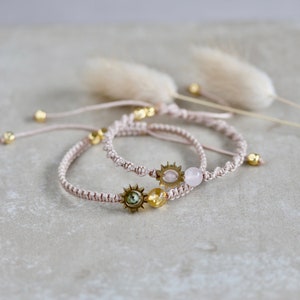 Può includere: Due braccialetti delicati con cordini regolabili, con piccoli ciondoli a forma di sole e perline di pietre preziose. Un braccialetto ha una pietra preziosa rosa, l'altro ha una pietra preziosa gialla.