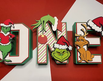 Op de afbeelding: Groene en rode kerstversiering met de Grinch, Max de hond en het woord "ONE".