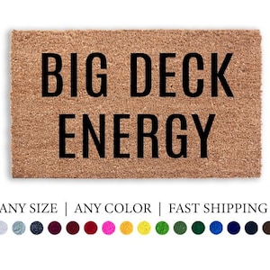 May include: A rectangular doormat made of natural coir fiber. The mat features the phrase "BIG DECK ENERGY" in bold, black capital letters. The words "Doormat Decor" are written in cursive at the top.