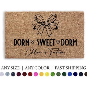 May include: A rectangular doormat with the text "DORM SWEET DORM" and the names "Chloe + Tatum" in black. A decorative bow graphic is above the text. The doormat is a natural tan color.