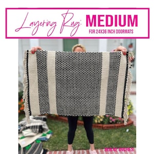 May include: A black and white striped rug with fringe on the edges. The rug is 30x42 inches and is being held up by a person. The text "Layering Rug: MEDIUM FOR 24X36 INCH DOORMATS" is at the top of the image.