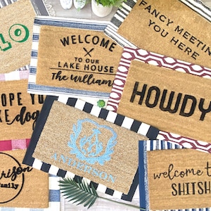 May include: A collection of ten doormats with various welcome messages and designs. The doormats are made of coir and have a variety of colors and patterns. Some of the messages include "Hello", "Welcome to our Lake House", "Fancy Meeting You Here", "Howdy", "I Hope You Like Dogs", "The Harrison Family", "Welcome to the Shit Show", and "PPENS".