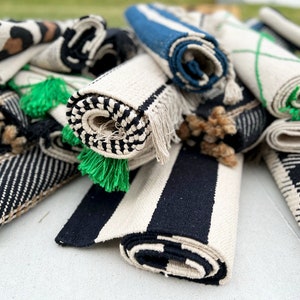 May include: A pile of rolled up rugs in various colors and patterns, including black and white stripes, brown and black animal print, and blue and white stripes. The rugs have green tassels.