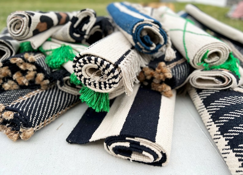 May include: A pile of rolled up rugs in various colors and patterns, including black and white stripes, brown and black animal print, and blue and white stripes. The rugs have green tassels.