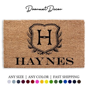 May include: A brown coir doormat with a black shield design featuring the letter "H" and the name "HAYNES" in black lettering.