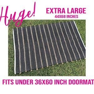 Op de afbeelding: Zwart-wit gestreept jutekleed met kwastjes. Het kleed is 44x68 inch en past onder een deurmat van 36x60 inch. "Huge!" en "EXTRA LARGE" staan in roze boven het kleed.