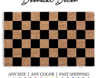 May include: Checkered doormat with black and brown squares. The doormat is made of coir and has a shaggy texture. The text "Doormat Decor" is written above the doormat.
