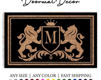 May include: A black doormat with a gold monogram design featuring a crown, lions, and the letter "M".