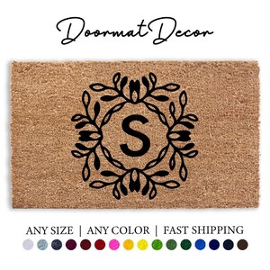 May include: A brown coir doormat with a black floral wreath design and the letter "S" in the center. The text "Doormat Decor" is at the top of the image. The text "ANY SIZE | ANY COLOR | FAST SHIPPING" is at the bottom of the image.