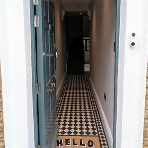 Puede incluir: Una puerta azul verdosa se abre a un pasillo con suelo de baldosas de ajedrez negro y blanco. Una alfombra de bienvenida con el texto "HELLO HELLO" está colocada en la entrada.