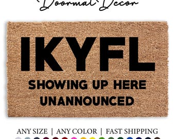 May include: A brown coir doormat with the text "IKYFL SHOWING UP HERE UNANNOUNCED" in black lettering.