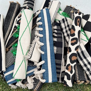 May include: A collection of rolled-up rugs with various patterns, including black and white stripes, black and white checkered, leopard print, and a geometric design with green accents. The rugs are made of natural fibers and have fringe edges.