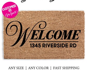 May include: A brown coir doormat with the text "WELCOME" in a black cursive font and the address "1345 RIVERSIDE RD" in black block letters. The doormat is customizable with different colors and sizes.
