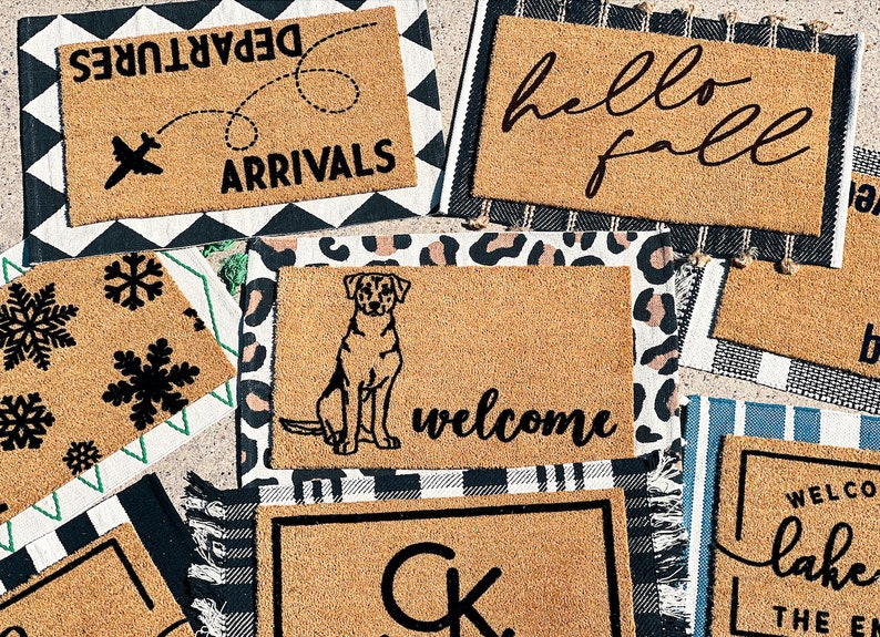 May include: A collection of eight doormats with various designs, including "Departures Arrivals", "Hello Fall", "Welcome", "Lake", and a dog silhouette. The doormats are made of coir and have a natural brown color.