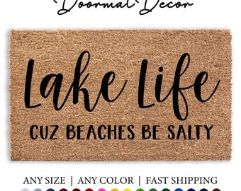May include: A brown coir doormat with the text "Lake Life Cuz Beaches Be Salty" in black lettering. The doormat is available in any size and color.