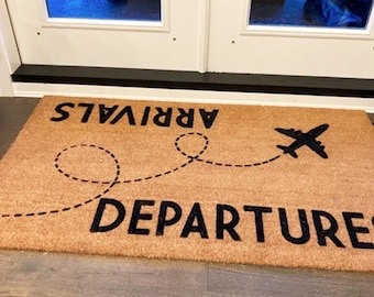 May include: A brown coir doormat with the words "ARRIVALS" and "DEPARTURE" printed in black. A black airplane silhouette is flying above a dotted line.