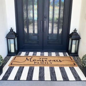 May include: A black and white striped doormat with the text "The Monsevais Family" in a cursive font on a brown coir mat.