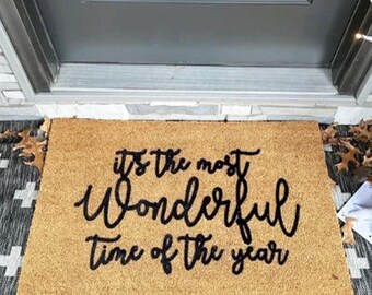 May include: A brown coir doormat with the text "It's the most wonderful time of the year" in black script lettering.