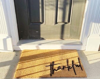 May include: A brown coir doormat with the word "thankful" written in black script.