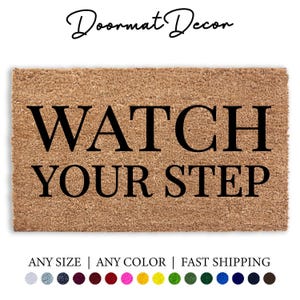 Puede incluir: Una alfombra de coco marrón con el texto "WATCH YOUR STEP" en letras negras.