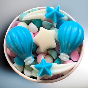 May include: A white bowl filled with blue, white and light blue candy melts shaped like stars, shooting stars and hot air balloons.