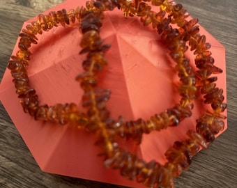 May include: Two amber necklaces made of small, irregular pieces of amber. The necklaces are displayed on a bright orange background.