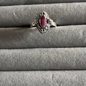 May include: A silver ring with a pink gemstone set in a detailed, ornate design.