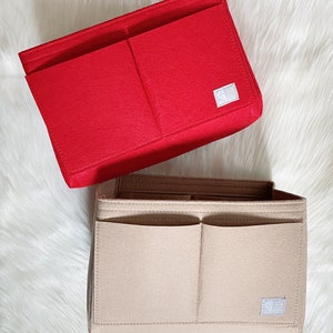 Pode incluir: Dois organizadores de bolsa de feltro, um vermelho e outro bege. Ambos os organizadores têm vários compartimentos e um pequeno logotipo quadrado no canto inferior direito.