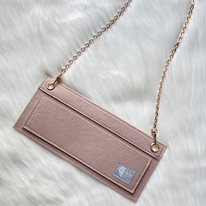 May include: A light pink felt pouch with a gold chain strap. The pouch has a diamond logo on the front and two pockets.